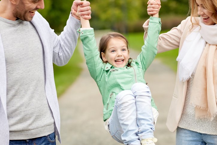 Parents happily swing their daughter between them outside